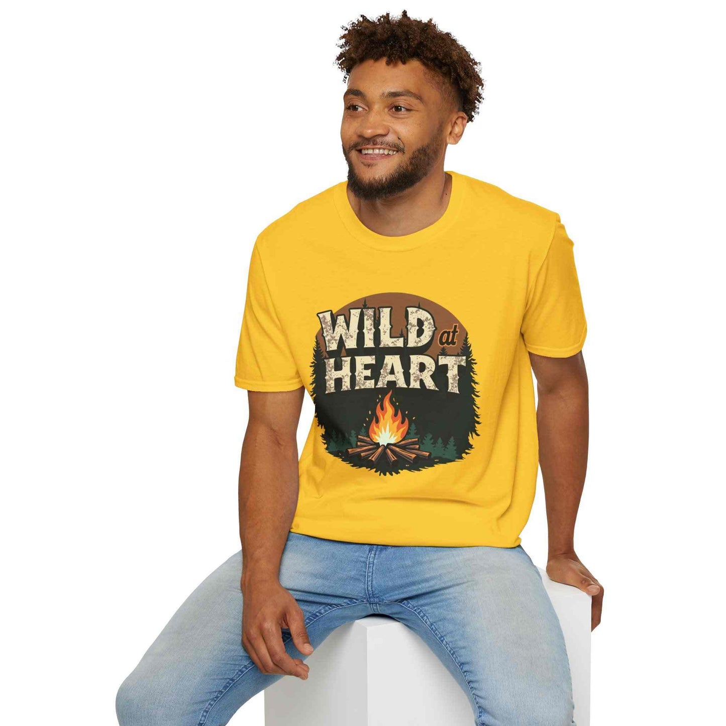 Man wearing yellow Wild at Heart Camping T-Shirt with campfire graphic sitting on white block