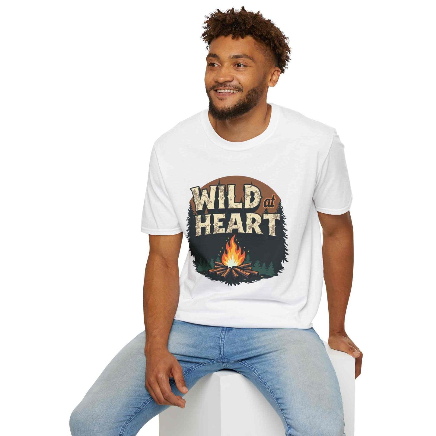 Man wearing white Wild at Heart Camping T-Shirt with campfire graphic and blue jeans sitting on white block