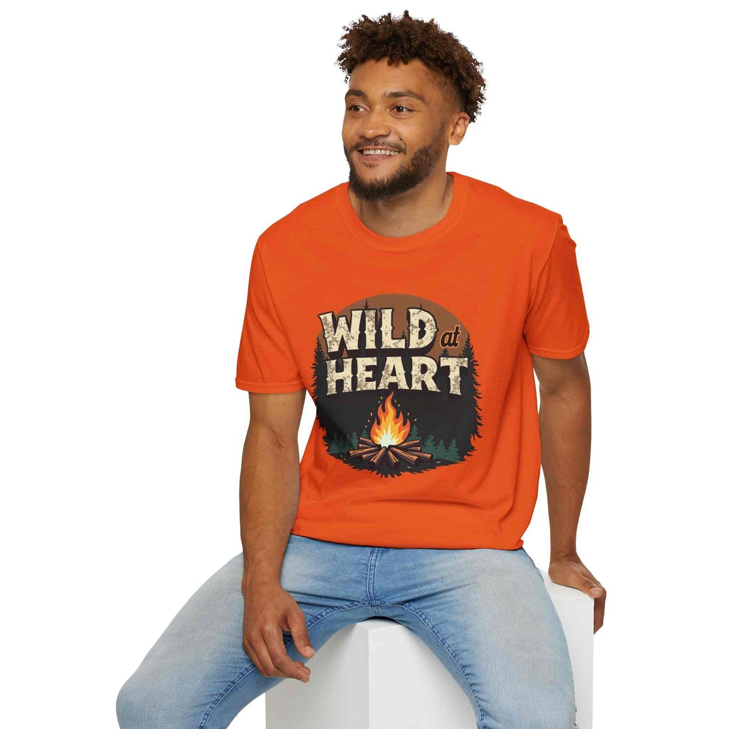 Man wearing orange Wild at Heart Camping T-Shirt with campfire graphic sitting on white block