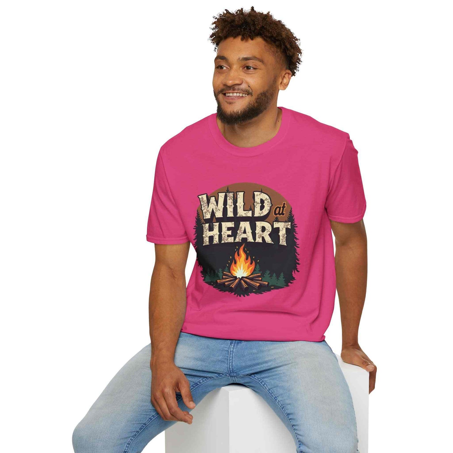 Man wearing pink Wild at Heart Camping T-Shirt with campfire graphic sitting on a white block