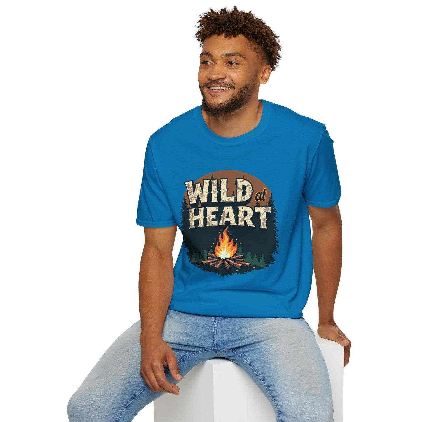 man wearing blue Wild at Heart Camping T-Shirt with campfire graphic sitting on white block