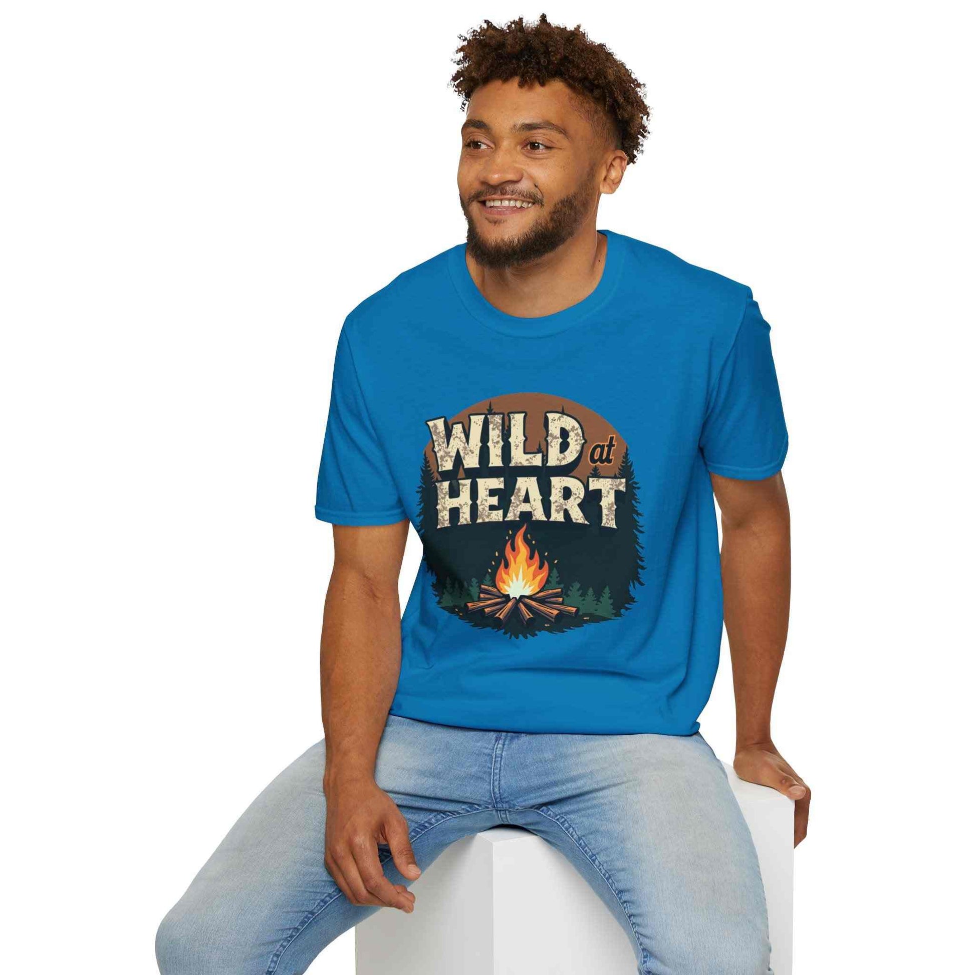 man wearing blue Wild at Heart Camping T-Shirt with campfire graphic sitting on white block